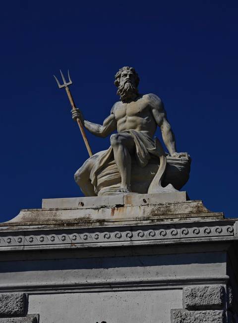       Sculpture of a muscular figure holding a staff against a clear sky.
  