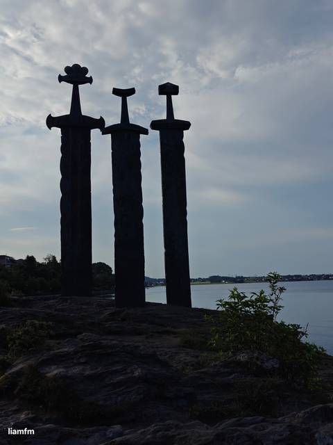       Silhouette of swords monument near the water during a cloudy day.
  