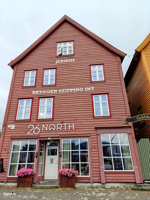       The exterior of a brown wooden building with signs for Bryggen Shipping Int and 26 North.
  