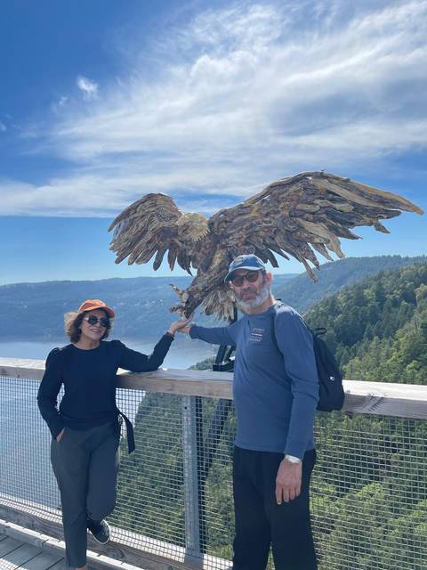 Two people posing with a large eagle statue in a scenic location.