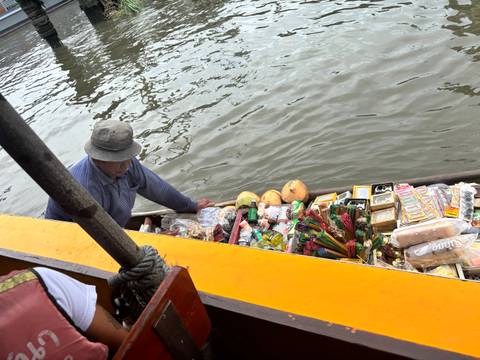 Vendor on a boat selling snacks and fruits on the water.