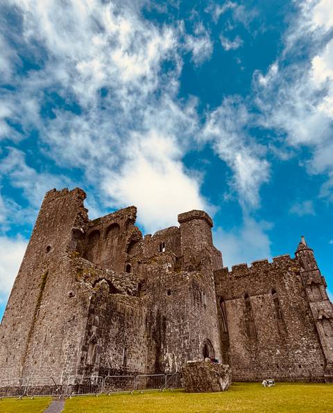 A historic stone castle against a blue sky with clouds.
