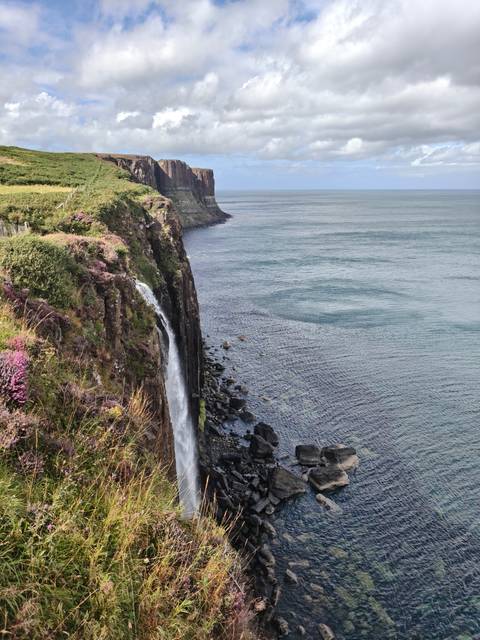 Coastal cliffs with a waterfall flowing into the ocean.