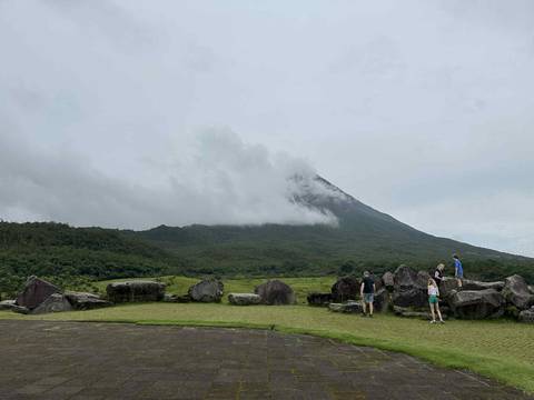 People exploring near a volcano under cloudy skies.