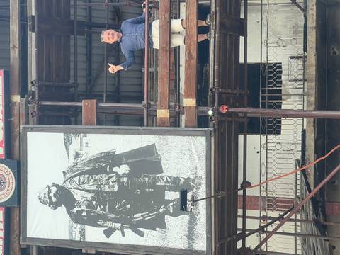       A man on a balcony next to a large poster.
  