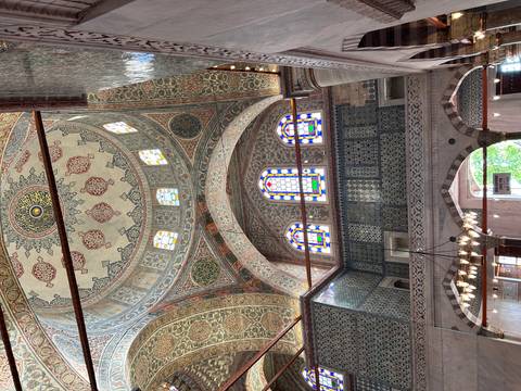       Decorated interior of a mosque with stained glass and tiles.
  