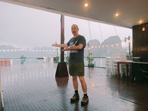       Man gesturing on a rainy deck with scenic cliffs.
  