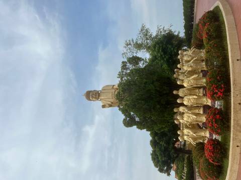 Golden statue surrounded by smaller statues and flowers.
