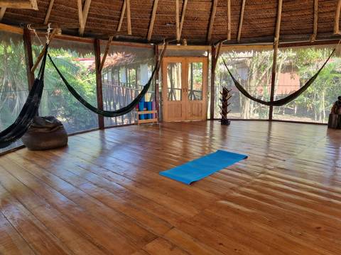       Open wooden room with hammocks and a yoga mat.
  