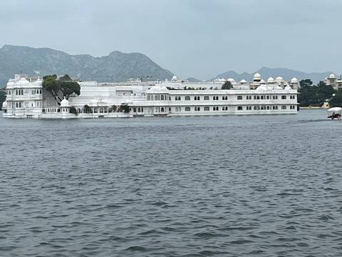 Large white palace on a lake with mountains in the background.