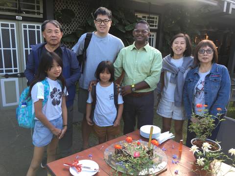 Group of people posing outdoors with flowers on a table.