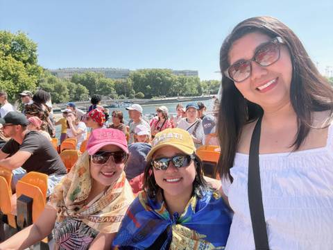       Three women on a boat ride with a river and city view.
  