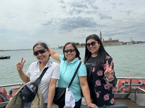 Three women posing on a water taxi with a view of Venice.