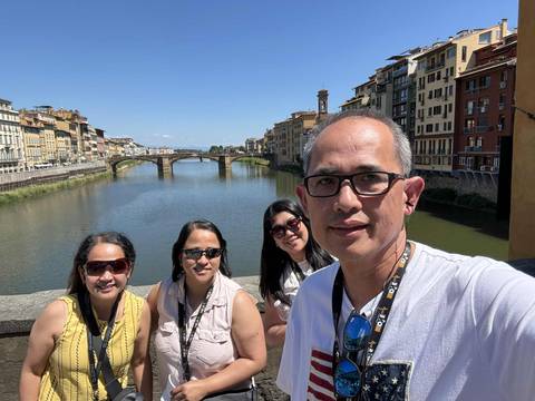       Group posing on a bridge with a scenic river view.
  