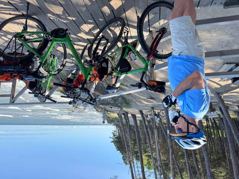 Person in cycling gear standing with bicycles, overlooking a scenic coastline.
