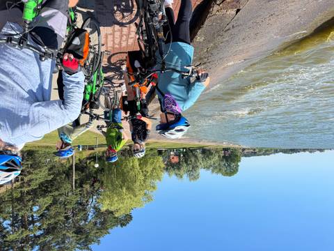 Group of people with bicycles by the water on a sunny day.