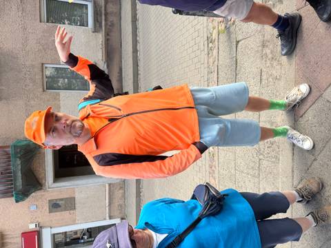 Man in an orange jacket making a gesture on a sidewalk.