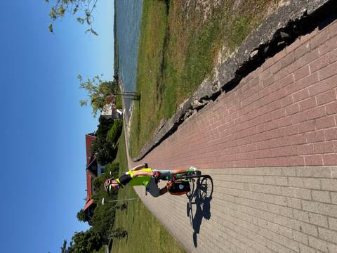 Cyclist on a paved path near a lake and houses.