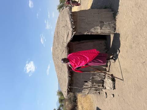 Man in traditional attire standing in front of a round hut.