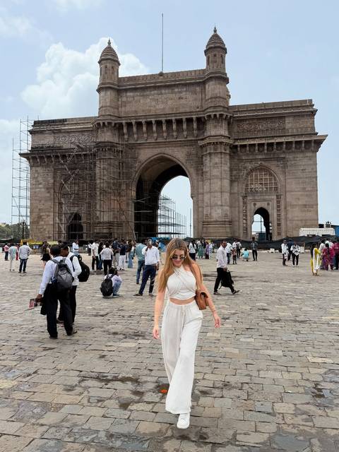       Person posing in front of the Gateway of India with a crowd.
  