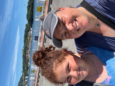 Two people smiling outdoors with a waterway and green hill in the background.