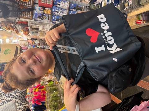       Person holding a bag with 'I Love Korea' text in a market.
  