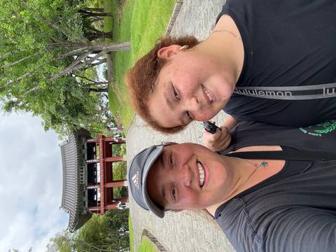       Two people smiling in front of a traditional building.
  