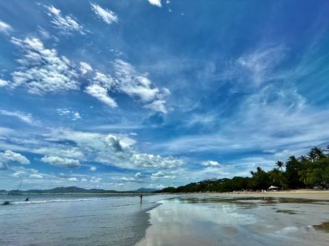 Wide view of a clear beach with scattered clouds in the sky.