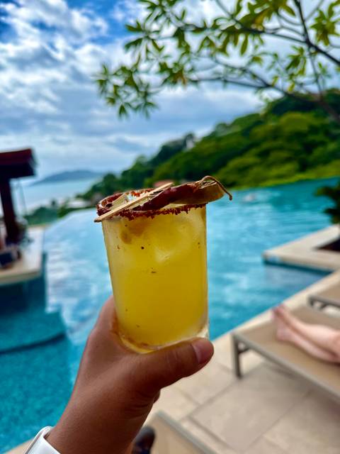 Close-up of a tropical drink by a pool with ocean view in the background.