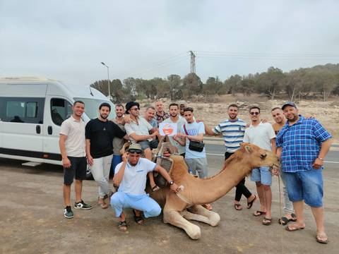       Men gathered around a camel with a desert backdrop.
  