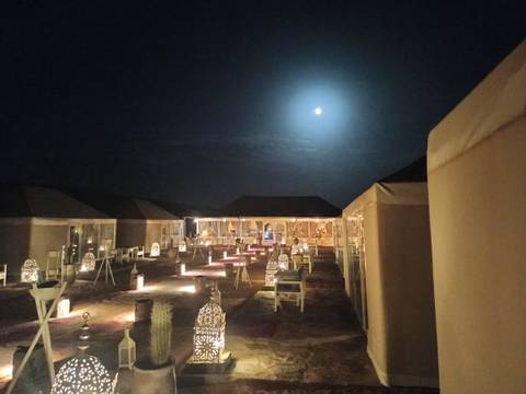 Night view of a desert camp with lit walkways and tents.