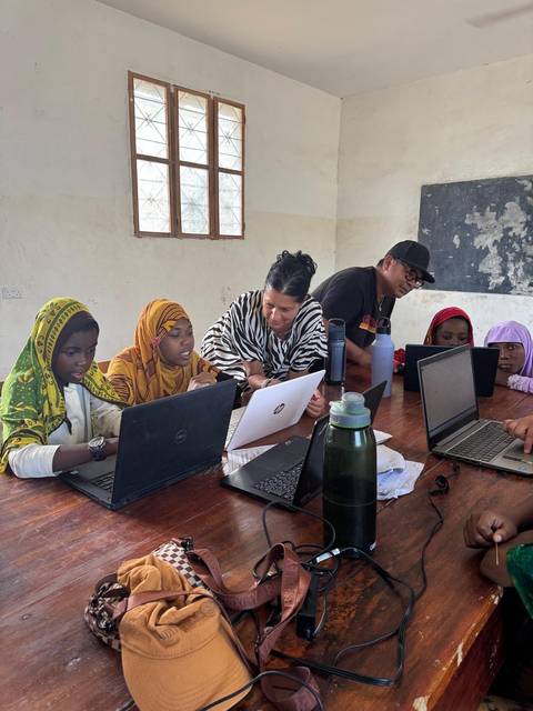 People sitting at a table with laptops in a classroom.