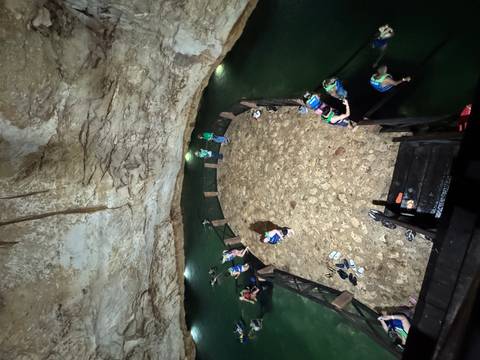 A group of people enjoying a swim in a cenote surrounded by rocky walls.