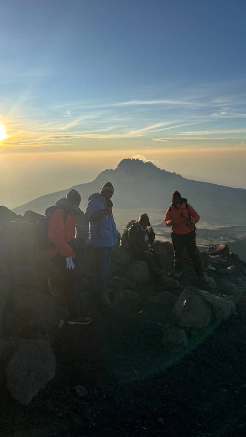       Group of hikers resting with a mountain backdrop at sunset.
  