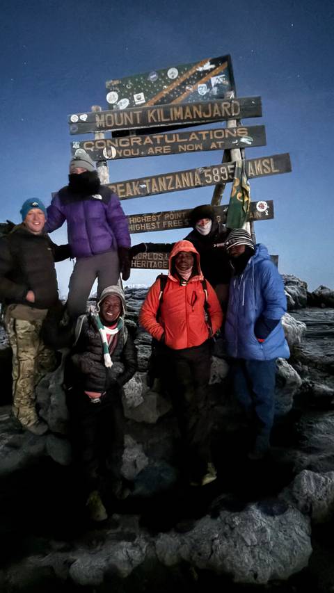       Group of hikers posing with summit sign at the highest point.
  