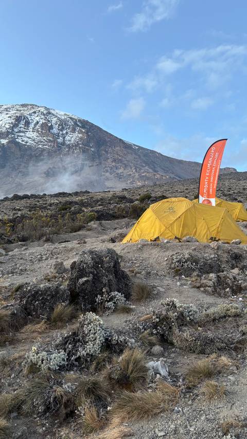       Tent camp on a rocky landscape with a mountain in the distance.
  