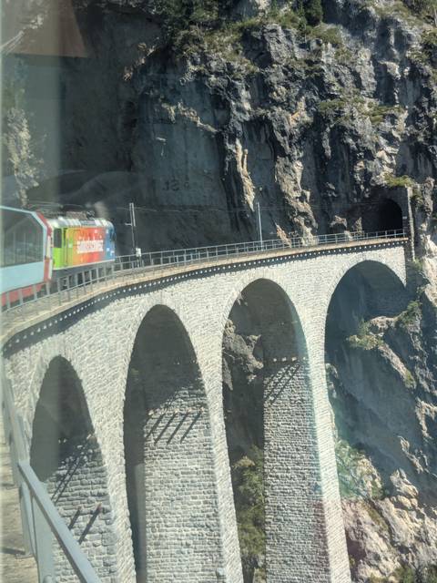       Colorful train crossing a stone bridge through a rocky landscape.
  