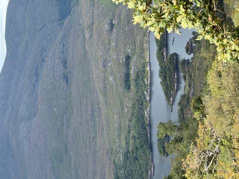 View of a lake surrounded by green hills and mountain backdrop.