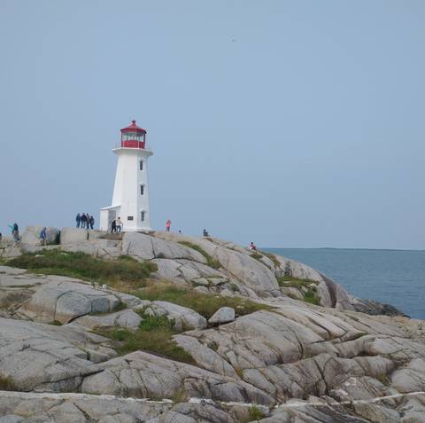 Iconic lighthouse on rocky coastline with people exploring.