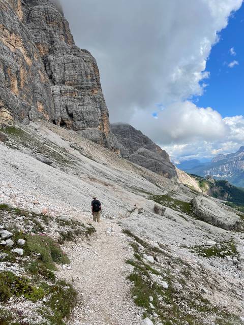 Person hiking on a rocky mountain trail with dramatic cliffs.