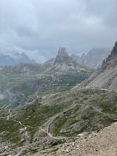 Pathway through rocky mountainous landscape with a distant lodge.