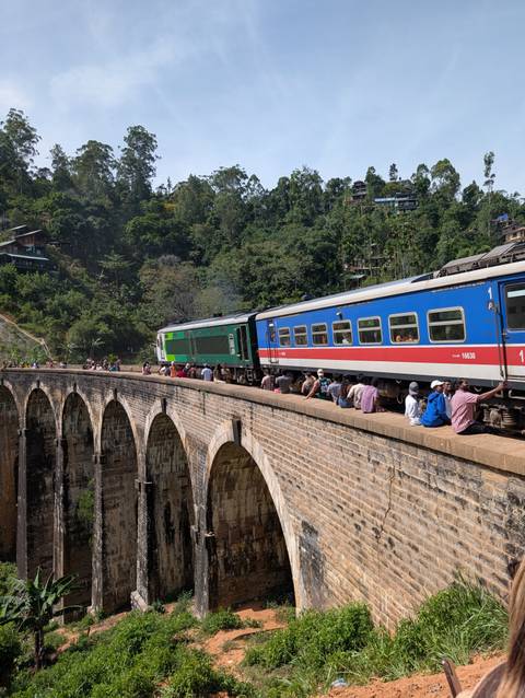 A train crossing a historic stone bridge with people sitting along the sides.