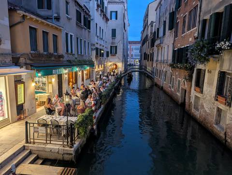 An evening canal scene in Venice with people dining by the water.