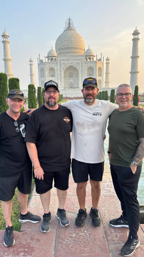 Four men posing for a photo with Taj Mahal blurred in the background.