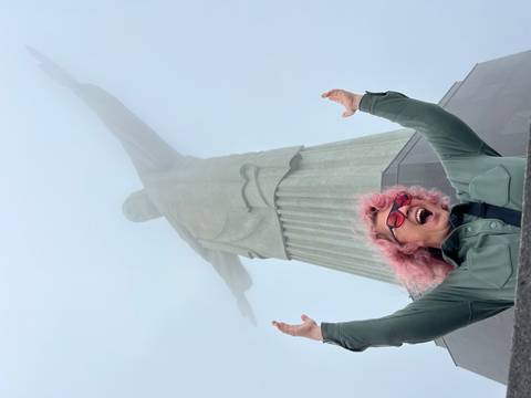       Person raising arms in front of a large statue in the mist.
  