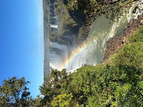       Rainbow over waterfalls with lush greenery.
  