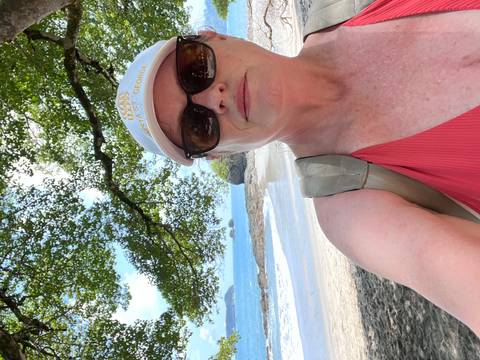 Woman taking a selfie at a beach with trees and water in the background.