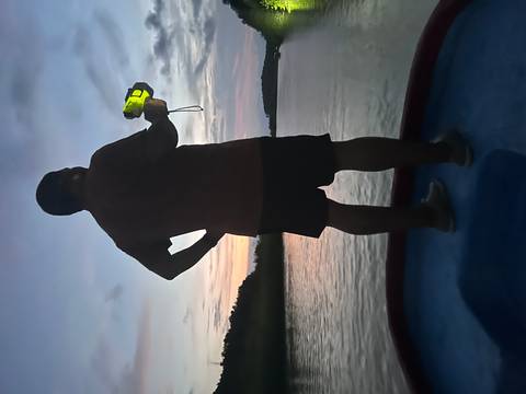       Silhouette of a person holding a camera against a sunset over water.
  