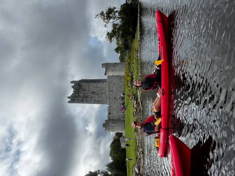       Two people kayaking on a lake with a historic castle in the background.
  
