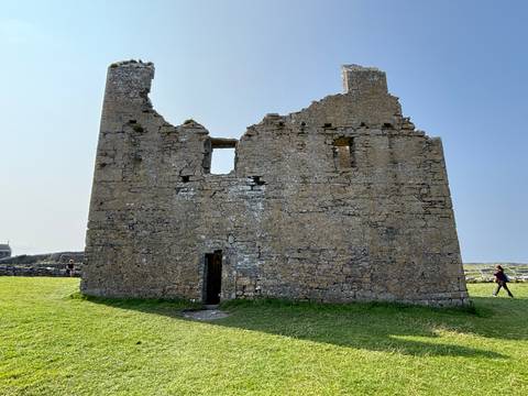       A stone building with a person jogging nearby on a sunny day.
  